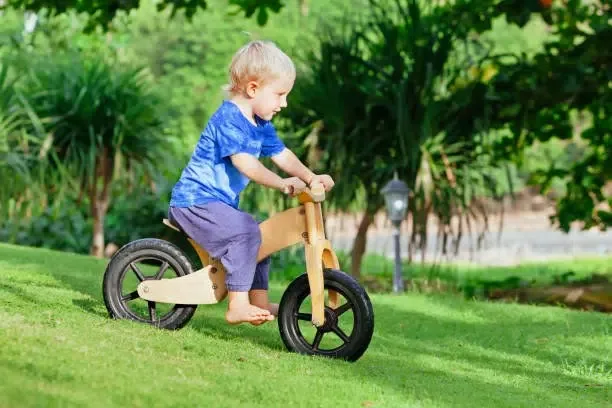 Un petit garçon jouant avec sa draisienne en bois dans le jardin