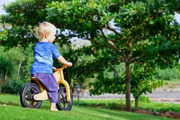 Garçon joyeux de 2 à 3 ans sur une draisienne en bois  Enfant heureux, pieds nus, apprenant à rouler et à garder l'équilibre sur un vélo d'entraînement dans le jardin.