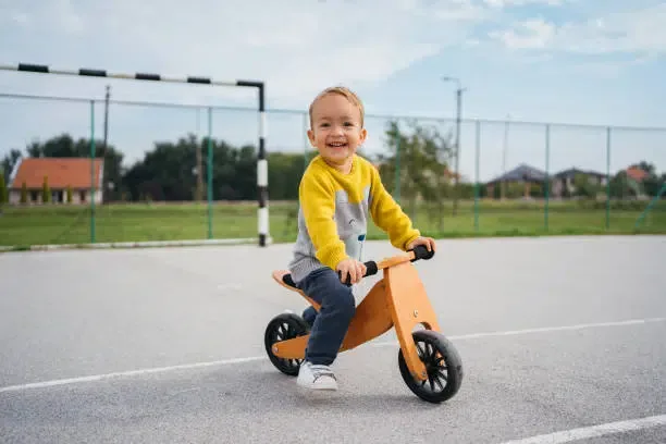 Un jeune garçon enjoué sur une draisienne en bois sur un terrain de sport.