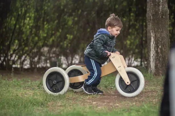 Jeune garçon faisant du vélo de type draisienne en bois,  par une belle journée de printemps dans le jardin.