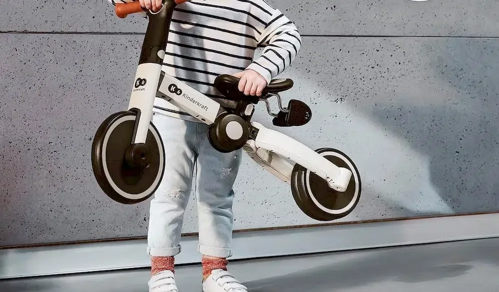 Un enfant tenant un tricycle Kinderkraft